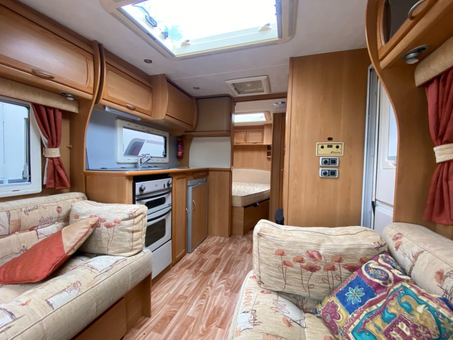 Interior of a caravan featuring a seating area, kitchenette, and sleeping space.