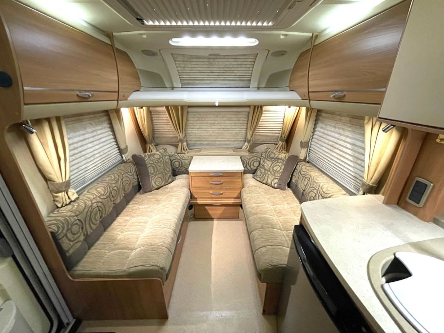 Interior of a caravan with lounge seating, dining table, and kitchen area.