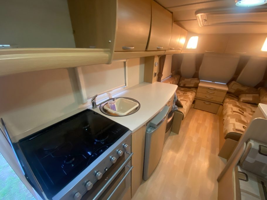 Interior of an RV kitchen with a modern stove, countertop, and seating area.