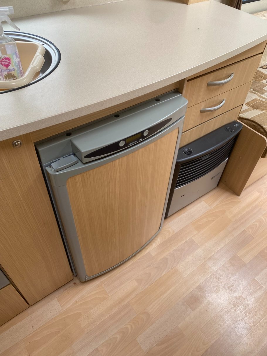 Compact kitchen area featuring a wood-effect fridge and two bins under the countertop.