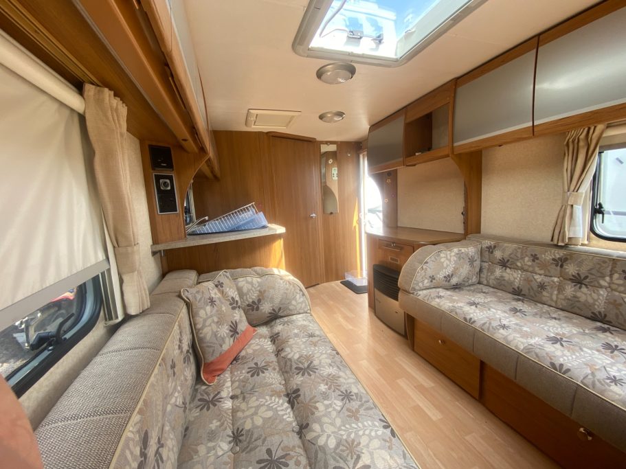 Interior of a caravan featuring wooden decor, sofas, and a bright skylight.