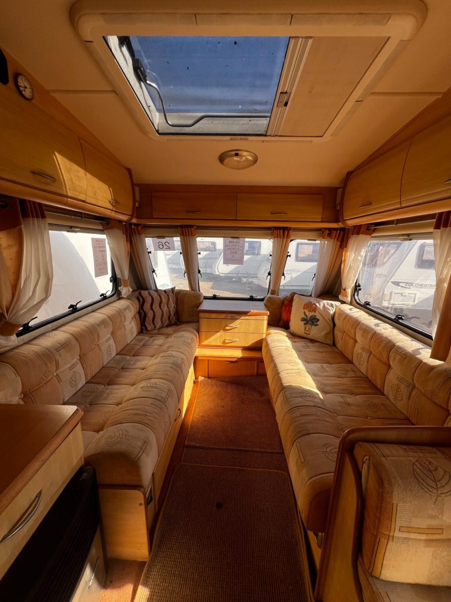 Interior of a caravan with soft furnishings and a skylight, featuring a central seating area.