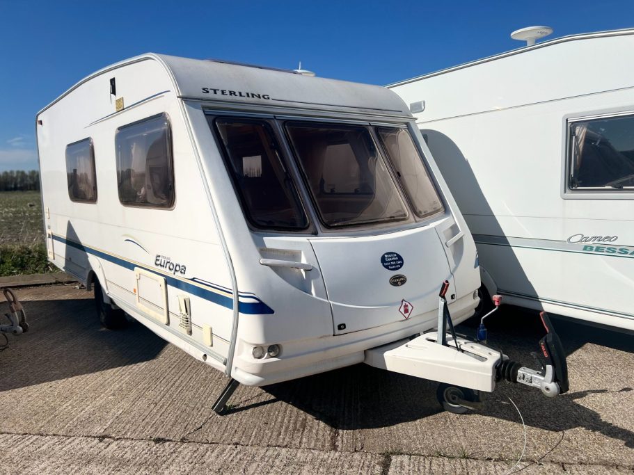 A white caravan parked on a paved area with clear blue skies above.