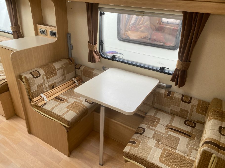 Interior of a caravan featuring a dining area with a table and cushioned seating.