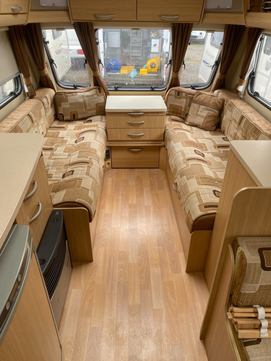 Interior of a caravan featuring seating, a table, and wooden flooring.