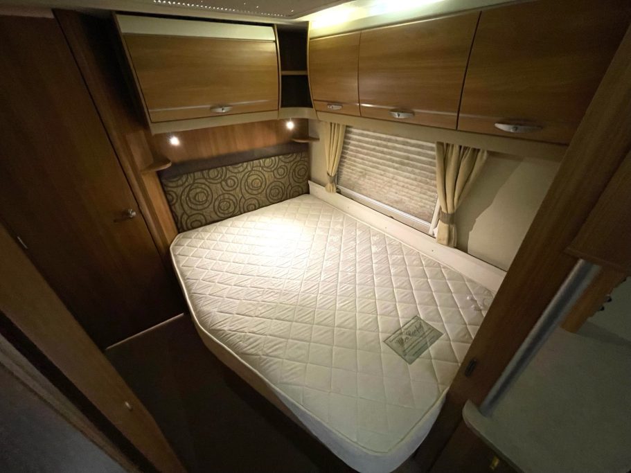Compact campervan interior featuring a double bed with wood cabinetry and soft lighting.